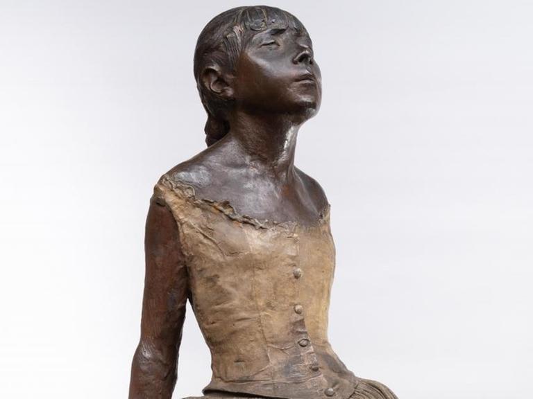 Eine Mädchen-Skulptur im Tanzrock verschränkt die Arme hinter dem Rücken.