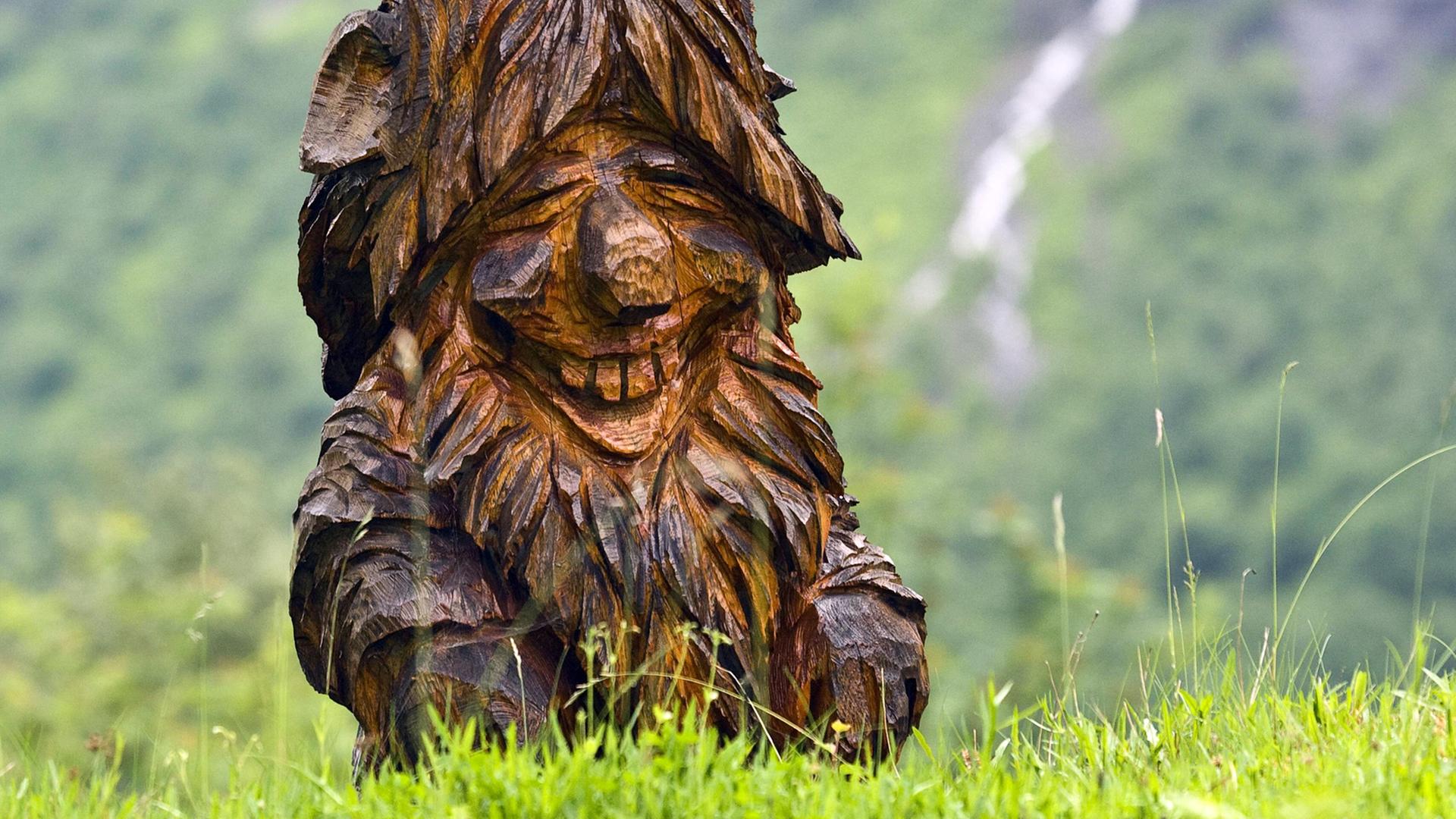 Ein aus Holz geschnitzter Troll in Norwegen auf einer Wiese.