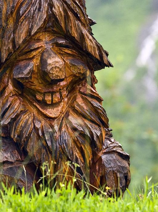 Ein aus Holz geschnitzter Troll in Norwegen auf einer Wiese.
