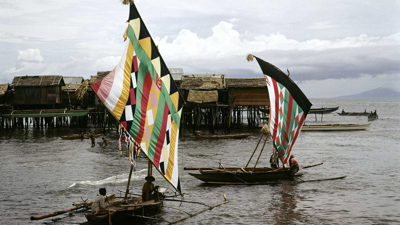 Zwei Auslegerboote mit bunten Segeln der Moro-Fischer, eine islamische Minderheit im Süden der Philippinen, fahren an einem Dorf in Pfahlbauweise bei Zamboanga auf der philippinischen Insel Mindanao vorbei. (Undatierte Aufnahme)