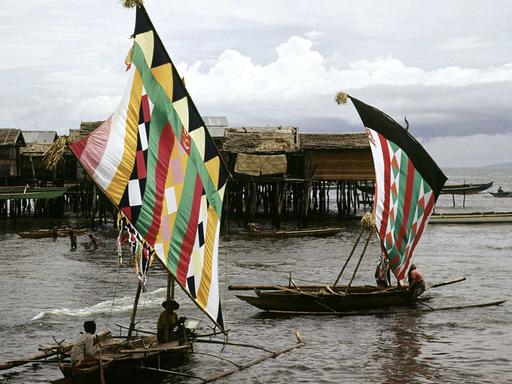 Zwei Auslegerboote mit bunten Segeln der Moro-Fischer, eine islamische Minderheit im Süden der Philippinen, fahren an einem Dorf in Pfahlbauweise bei Zamboanga auf der philippinischen Insel Mindanao vorbei. (Undatierte Aufnahme)