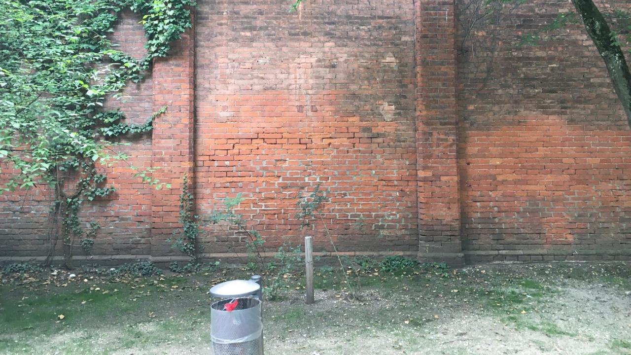 Eine leere Mauer umrahm von Bäumen im Münchner Glockenbachviertel.