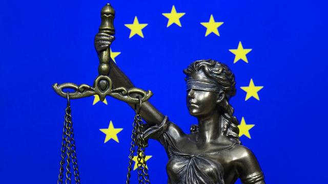 Eine Figur der Justitia vor der Fahne der Europäischen Union.