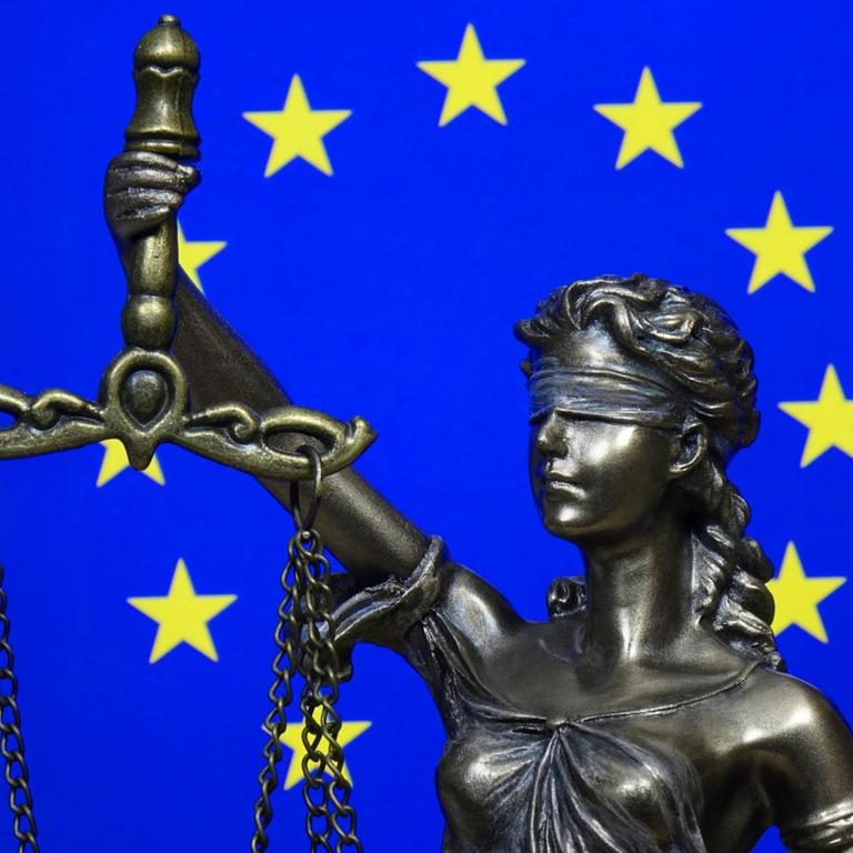 Eine Figur der Justitia vor der Fahne der Europäischen Union.