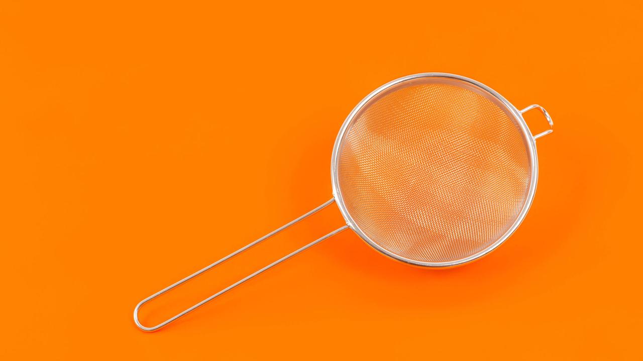 Küchensieb aus Metall vor orangenem Hintergrund Küchensieb aus Metall vor orangenem Hintergrund