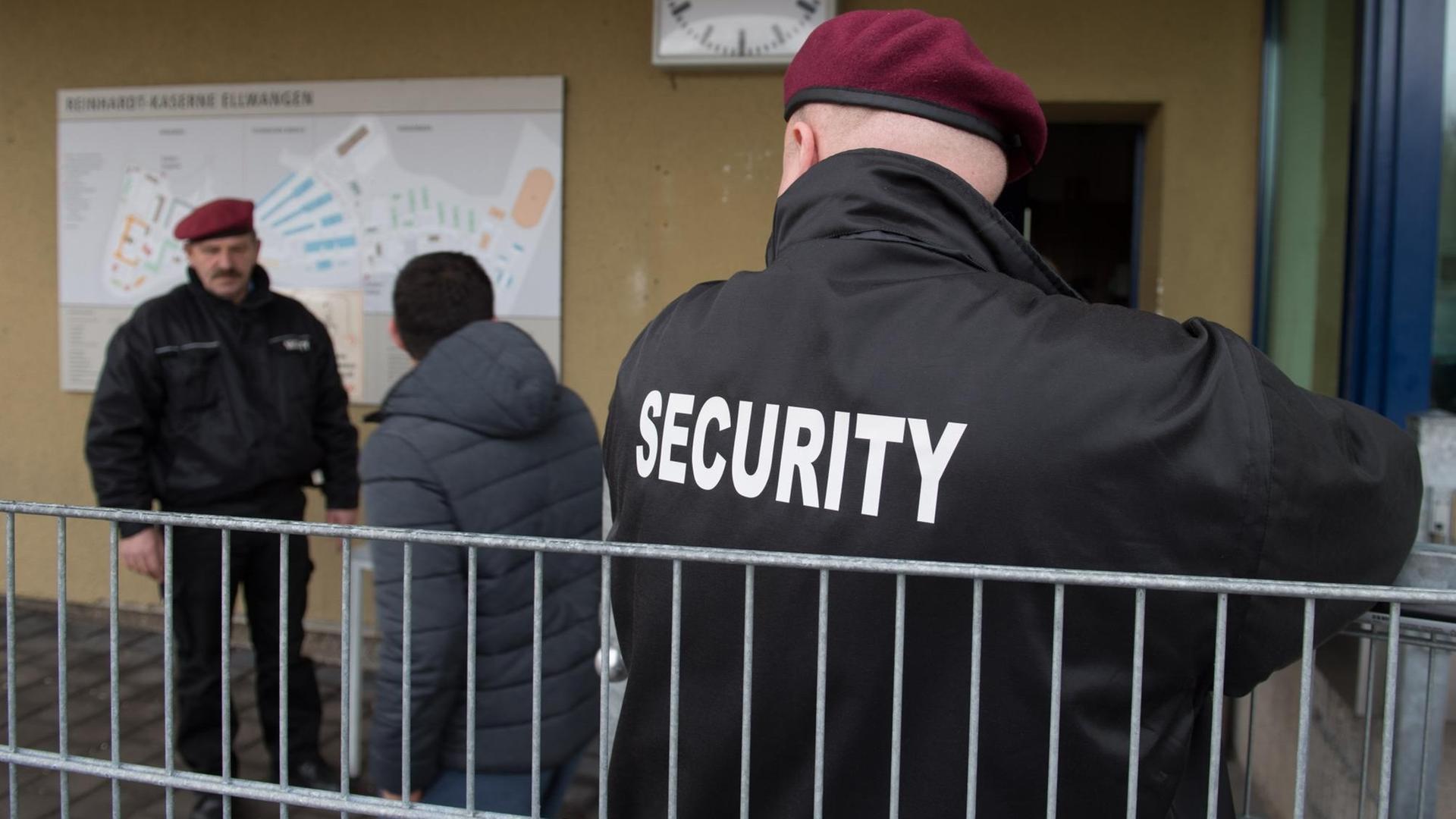Zwei Sicherheitskräfte des Sicherheitsdienstleisters Siba Security GmbH, stehen im Februar in der Landeserstaufnahmeeinrichtung (LEA) in der Reinhardt-Kaserne in Ellwangen (Baden-Württemberg) an der Pforte, in der Mitte geht ein Flüchtling vorbei. Zwei Sicherheitskräfte des Sicherheitsdienstleisters Siba Security GmbH, stehen im Februar in der Landeserstaufnahmeeinrichtung (LEA) in der Reinhardt-Kaserne in Ellwangen (Baden-Württemberg) an der Pforte, in der Mitte geht ein Flüchtling vorbei.