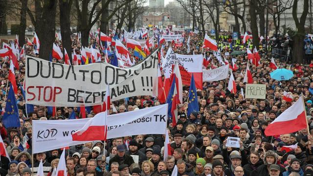 Sehr viele Menschen demonstrieren gegen die Regierung. Sie halten Banner und polnische Flaggen hoch.