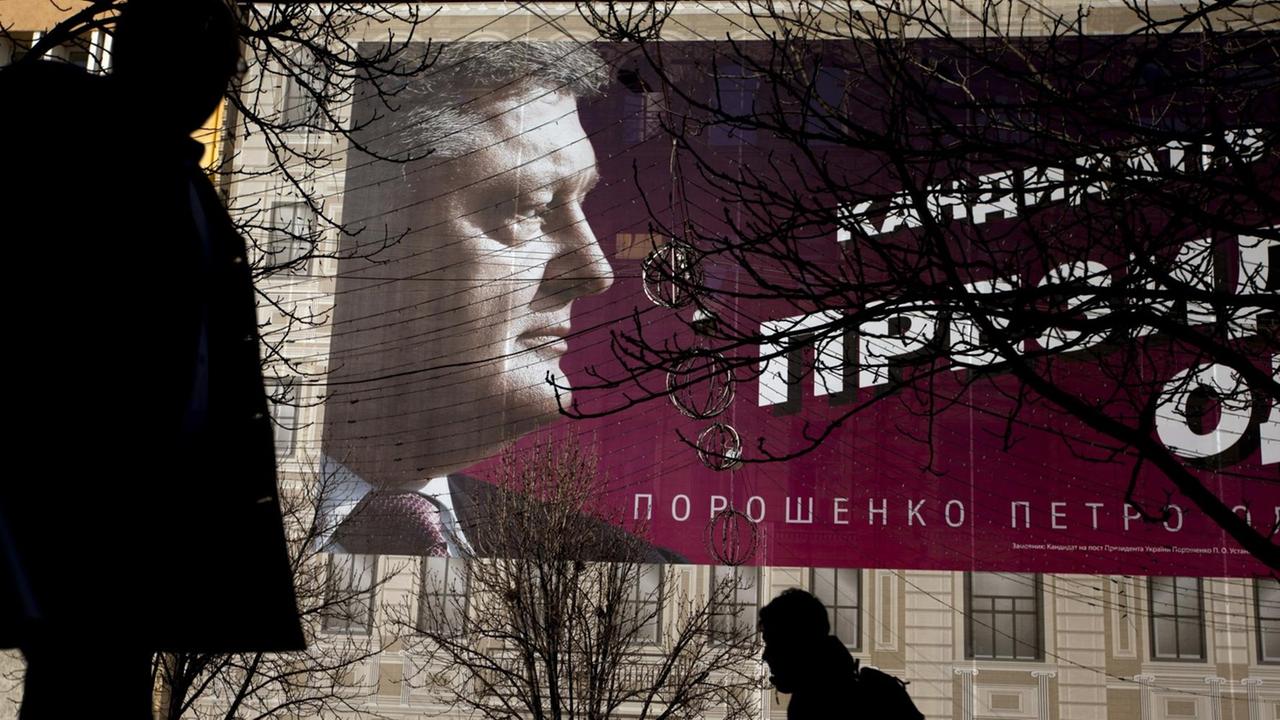 Fußgänger gehen an einem Plakat von Petro Poroschenko an einer Hauswand vorbei. 