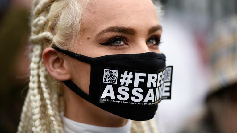 Eine Frau trägt eine Maske, auf der "Freiheit für Assange" steht.