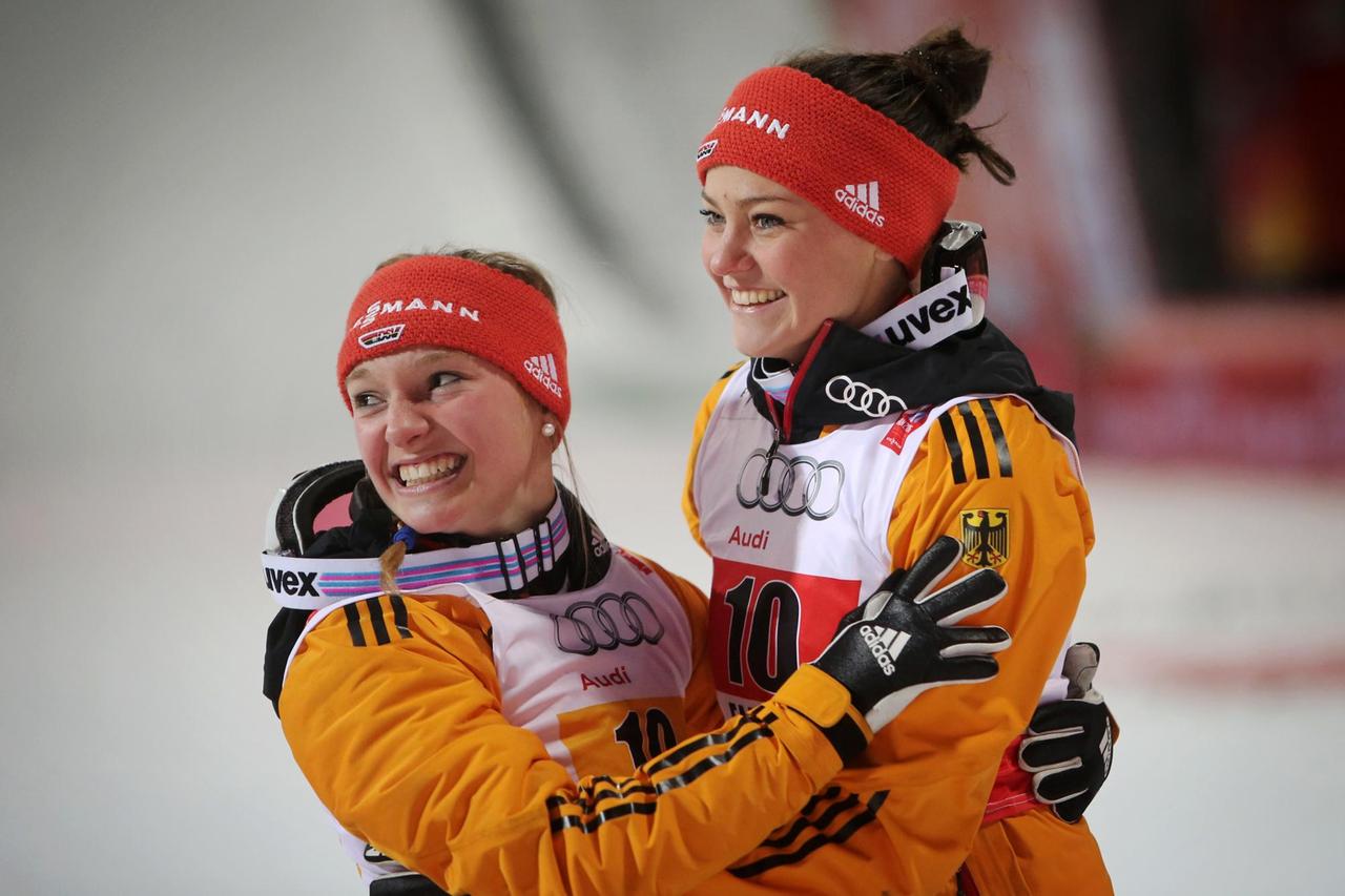 Zu sehen sind die Skispringerinnen Katharina Althaus und Carina Vogt, die sich freudestrahlend in die Arme fallen.