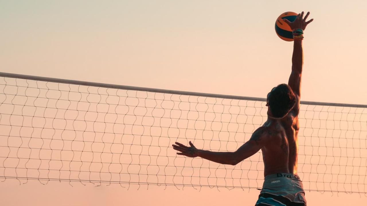 Abendliche Strandstimmung mit einem einzelnen Volleyballspieler, der am Netz hochspringt, um einen Ball zu schlagen. Abendliche Strandstimmung mit einem einzelnen Volleyballspieler, der am Netz hochspringt, um einen Ball zu schlagen.