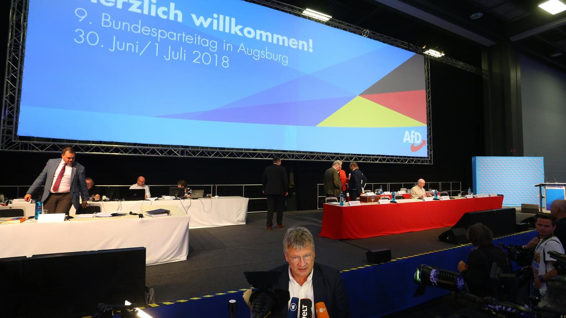 Jörg Meuthen, der Co-Parteivorsitzende der AfD, spricht beim Bundesparteitag vor Mikrofonen mit Journalisten. Im Hintergrund steht auf einer Leinwand "Herzlich Willkommen".