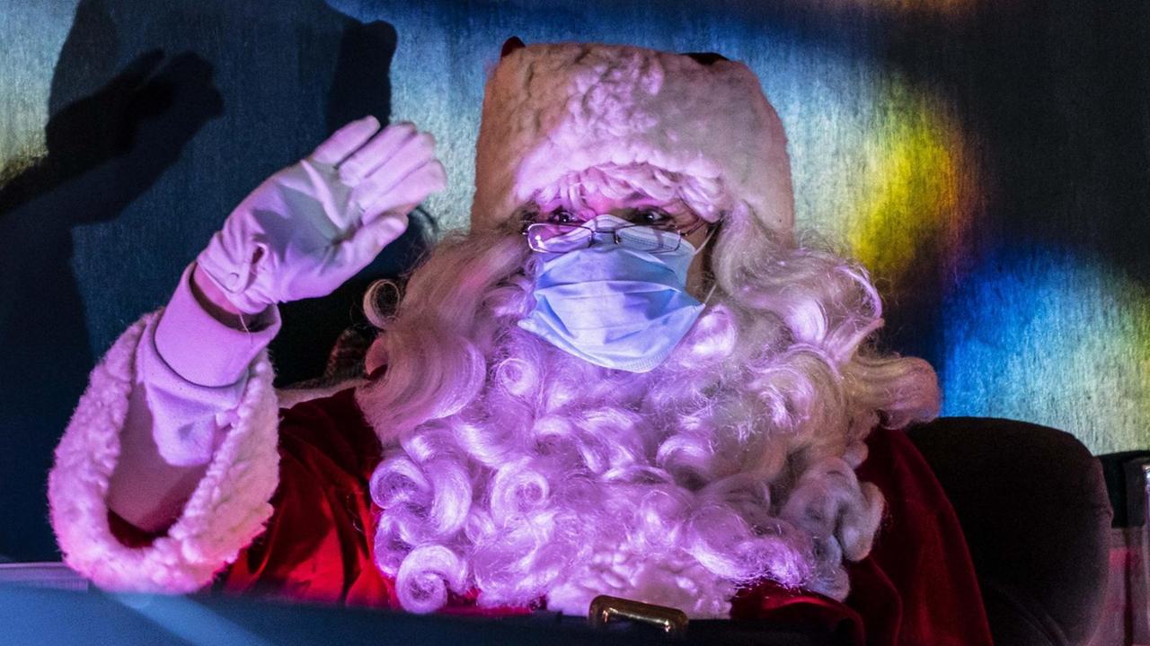 Ein verkleideter Weihnachtsmann mit Covidmaske winkt in einem drive-through Christmas event in Seattle, USA. Ein verkleideter Weihnachtsmann mit Covidmaske winkt in einem drive-through Christmas event in Seattle, USA.