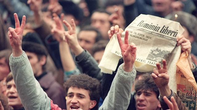 Tausende Rumänen jubeln am 24. Dezember 1989 in den Straßen von Bukarest. In der Zeitung ist zu lesen, dass Diktator Ceausescu und seine Frau verhaftet wurden.