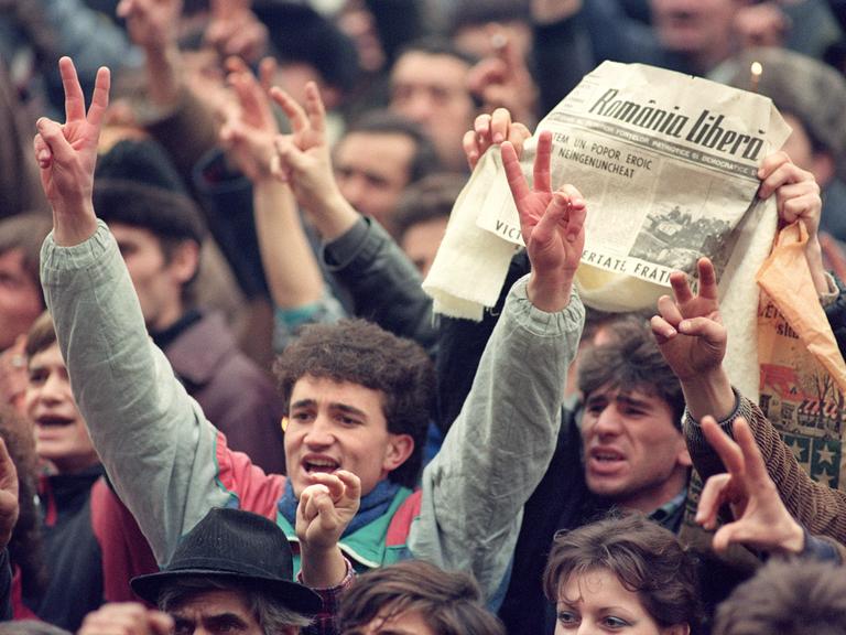 Tausende Rumänen jubeln am 24. Dezember 1989 in den Straßen von Bukarest. In der Zeitung ist zu lesen, dass Diktator Ceausescu und seine Frau verhaftet wurden.