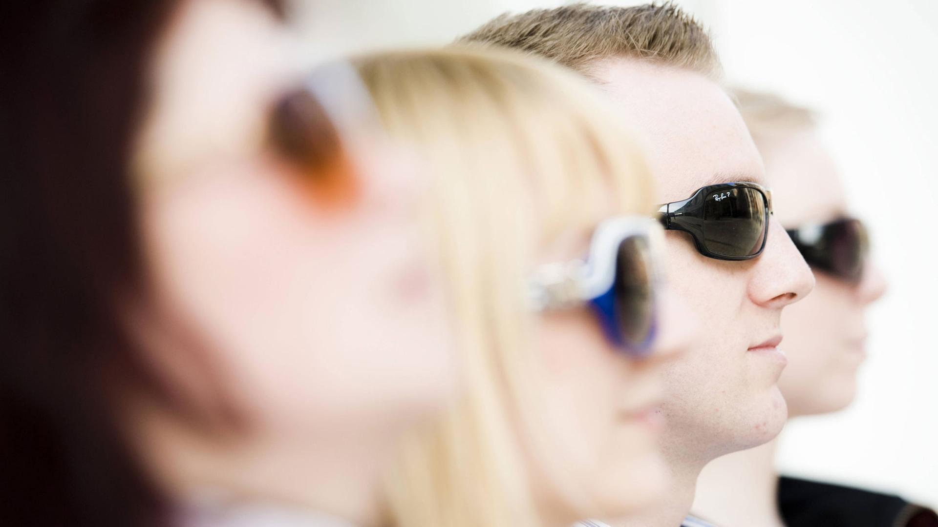Vier junge Menschen mit Sonnenbrillen sitzen in einer Reihe. Vier junge Menschen mit Sonnenbrillen sitzen in einer Reihe.