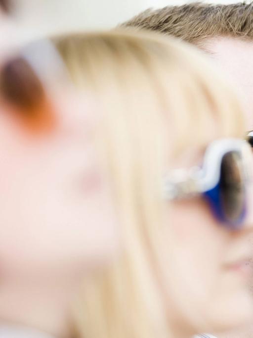 Vier junge Menschen mit Sonnenbrillen sitzen in einer Reihe.