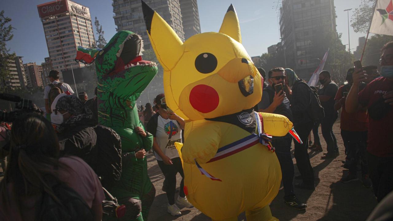 Als Dinosaurier und Pikachu verkleidete Demonstranten nehmen an einem regierungsfeindlichen Protest auf der Plaza de la Dignidad teil. Als Dinosaurier und Pikachu verkleidete Demonstranten nehmen an einem regierungsfeindlichen Protest auf der Plaza de la Dignidad teil.