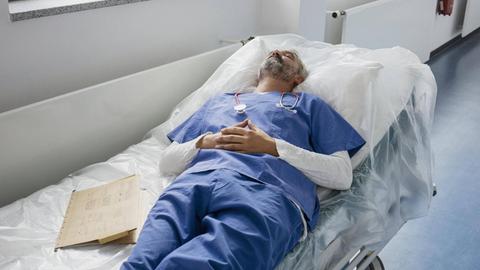 Ein erschöpfter Arzt liegt auf der Liege in einem Krankenhausflur und schläft.