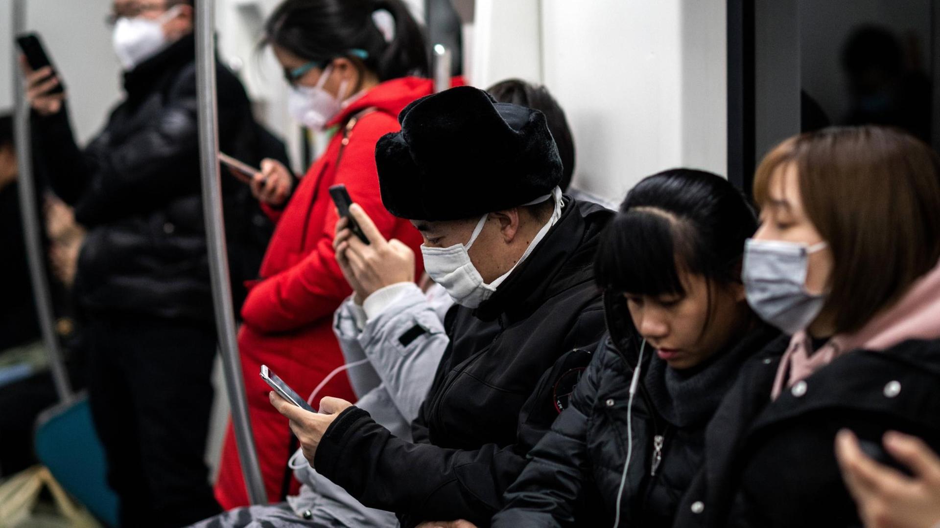 Menschen in einer U-Bahn in Peking. Sie tragen Mundschutz und schauen auf ihre Handys. Menschen in einer U-Bahn in Peking. Sie tragen Mundschutz und schauen auf ihre Handys.