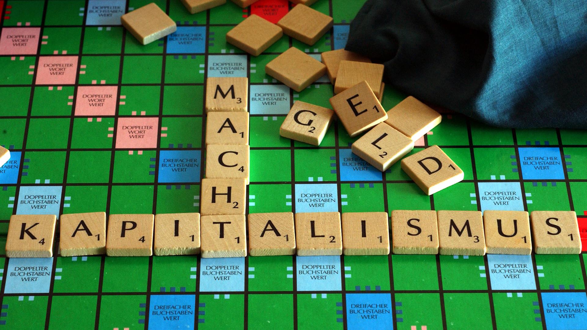 Auf einem Scrabble-Brett sind mit Buchstaben-Steinen die Begriffe "Kapitalismus" und "Macht" zusammengefügt, scheinbar wahllos im Hintergrund liegende Steine bilden das Wort "Geld". Auf einem Scrabble-Brett sind mit Buchstaben-Steinen die Begriffe "Kapitalismus" und "Macht" zusammengefügt, scheinbar wahllos im Hintergrund liegende Steine bilden das Wort "Geld".