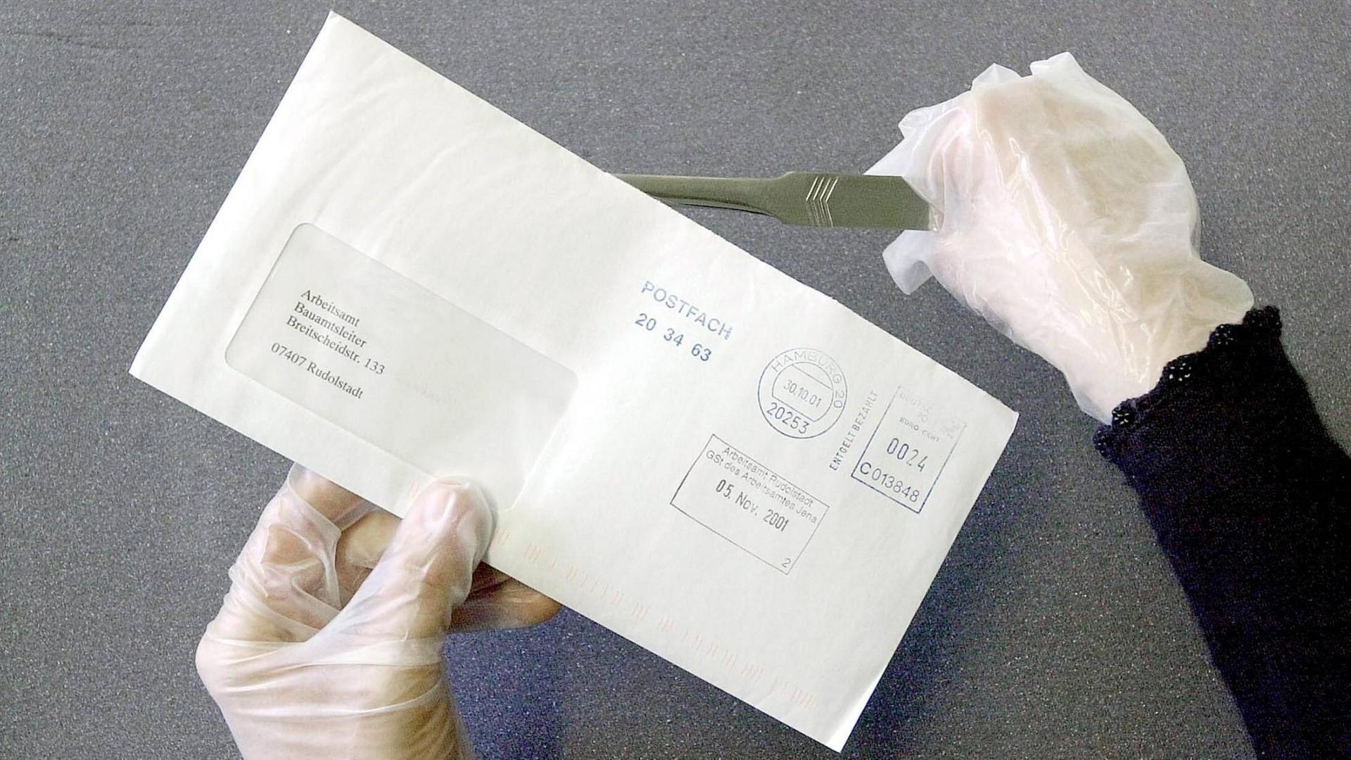 Eine Frau mit Handschuhen öffnet mit einem Brieföffner einen Umschlag adressiert an das Arbeitsamt.