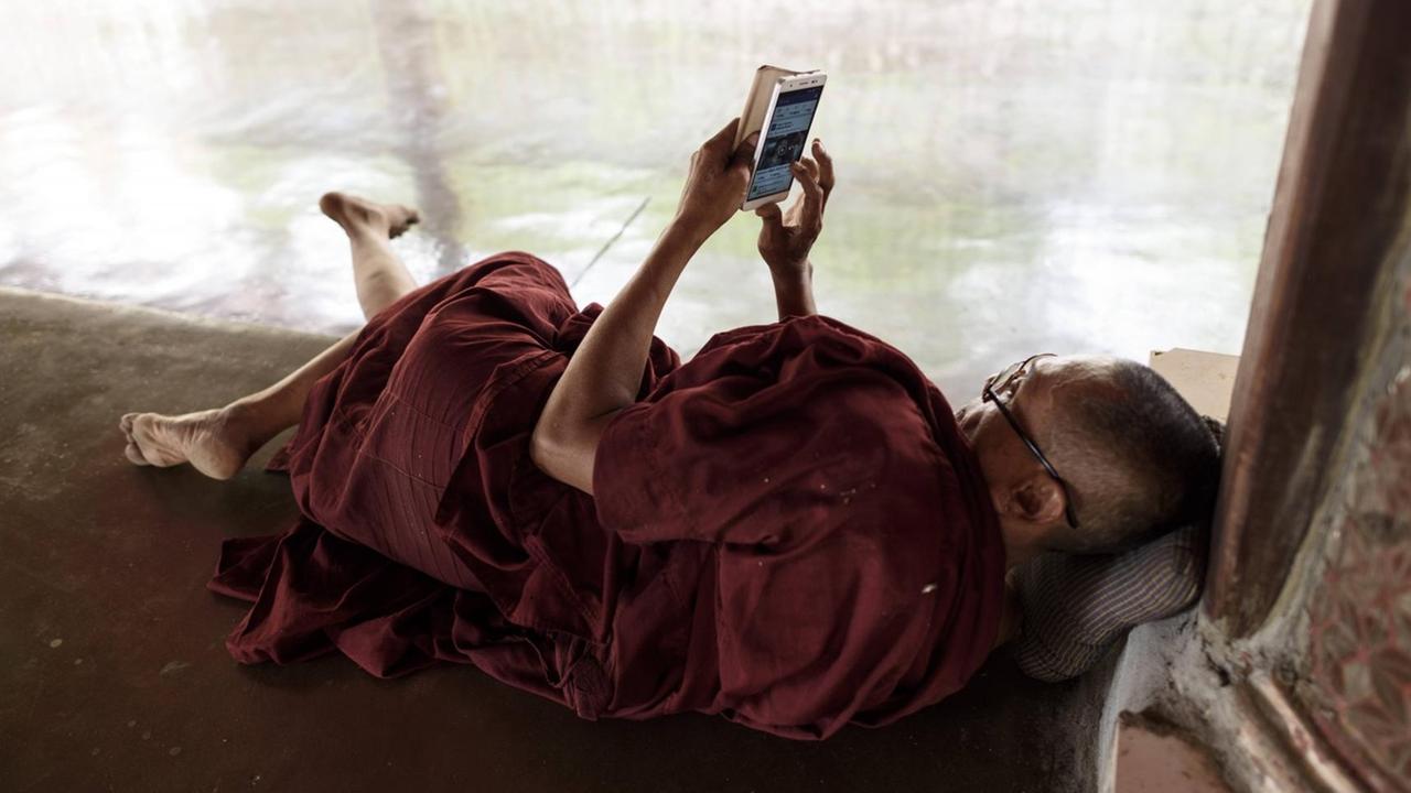 Ein buddhistischer Mönche besucht die Seite von Facebook auf seinem Samrtphone in der Kawhnat Pagode - Kor Nat, Myanmar, 2017 Ein buddhistischer Mönche besucht die Seite von Facebook auf seinem Samrtphone in der Kawhnat Pagode - Kor Nat, Myanmar, 2017