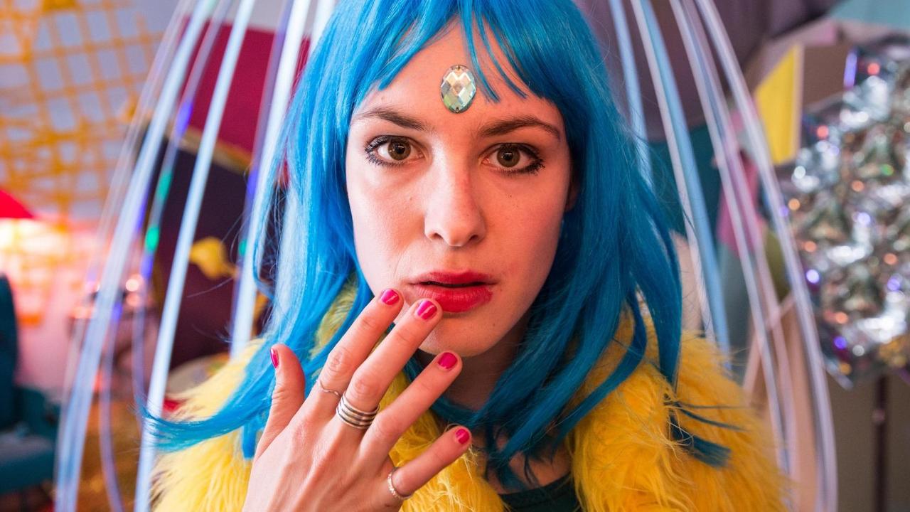 Eine Frau mit poppiger Kleidung und blauen Haaren blickt in die Kamera. Eine Frau mit poppiger Kleidung und blauen Haaren blickt in die Kamera.