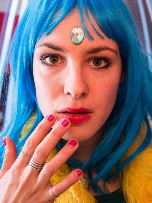 Eine Frau mit poppiger Kleidung und blauen Haaren blickt in die Kamera.