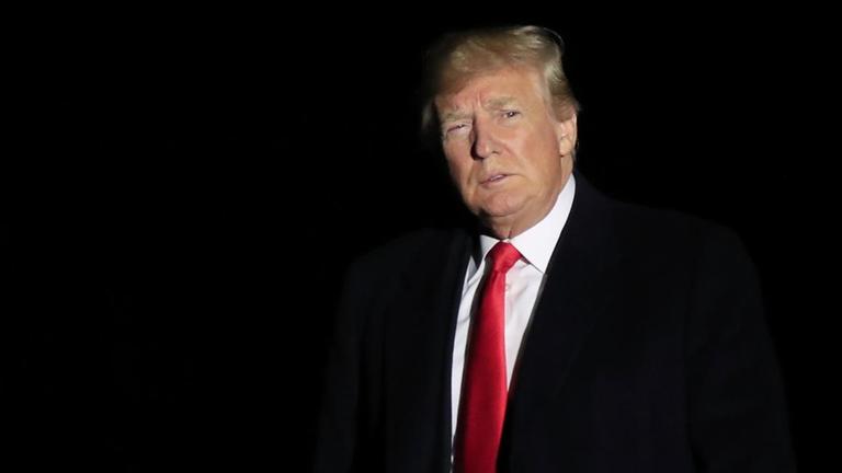 Donald Trump steht im Dunkeln vor dem Weißen Haus