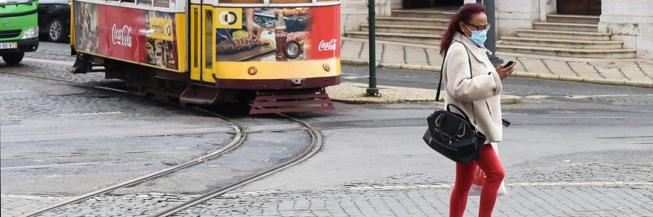 Frau mit Mund-Nasen-Bedeckung vor Straßenbahn in Lissabon.