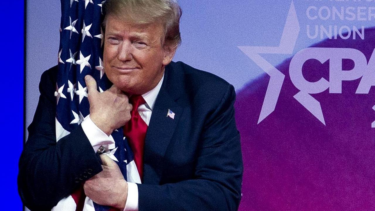 US-Präsident Donald Trump steht auf einer Bühne und umarmt eine amerikanische Staatsflaage. US-Präsident Donald Trump steht auf einer Bühne und umarmt eine amerikanische Staatsflaage.