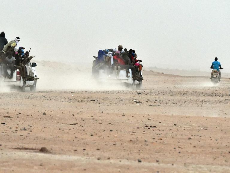 Mehrere Pick-ups, auf denen dutzende Migranten sitzen, fahren durch die Wüste von Agadez im Niger in Richtung Liyben (1.6.2015).