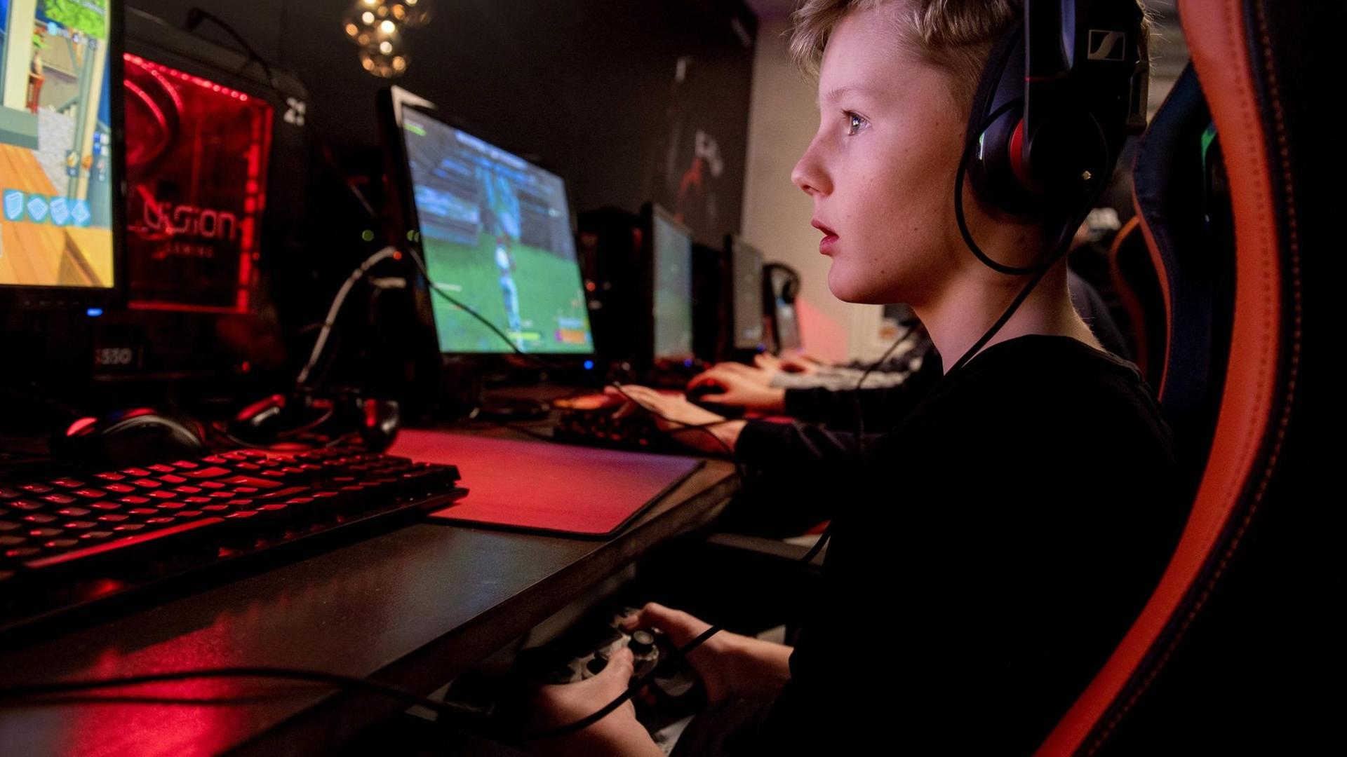 Ein Junge sitzt vor einem Computermonitor und spielt das Spiel "Fortnite". Sein Blick ist gefesselt und in der Hand hält er eine Fernbedienung. Ein Junge sitzt vor einem Computermonitor und spielt das Spiel "Fortnite". Sein Blick ist gefesselt und in der Hand hält er eine Fernbedienung.