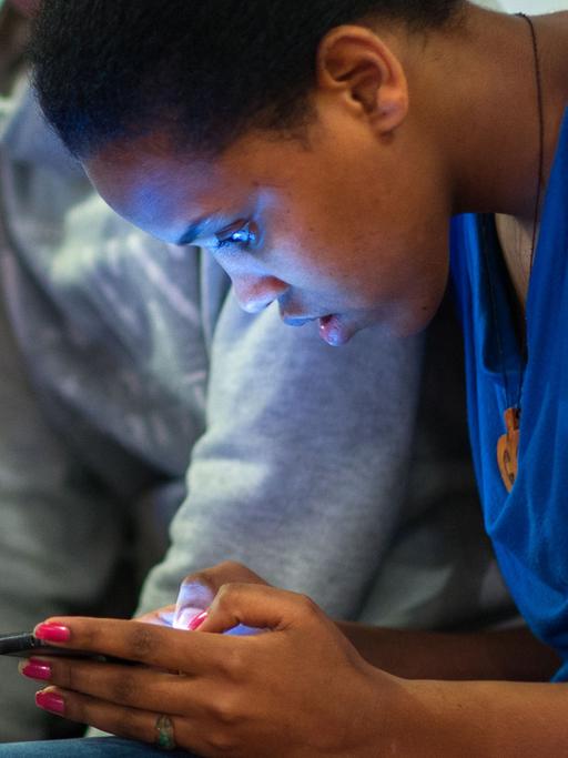 Eine 16-Jährige liest im Klassenraum Nachrichten auf ihrem Smartphone.