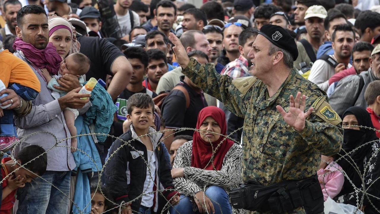 Ein mazedonischer Offizier spricht mit Flüchtlingen die jenseits der mazedonischen Grenze auf griechischem Terrain auf die Einreise warten 