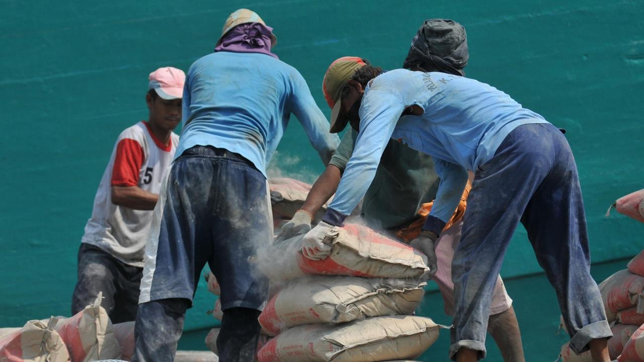 Eine Gruppe von Arbeiter stapeln Zementsäcke vor einem Schiff.