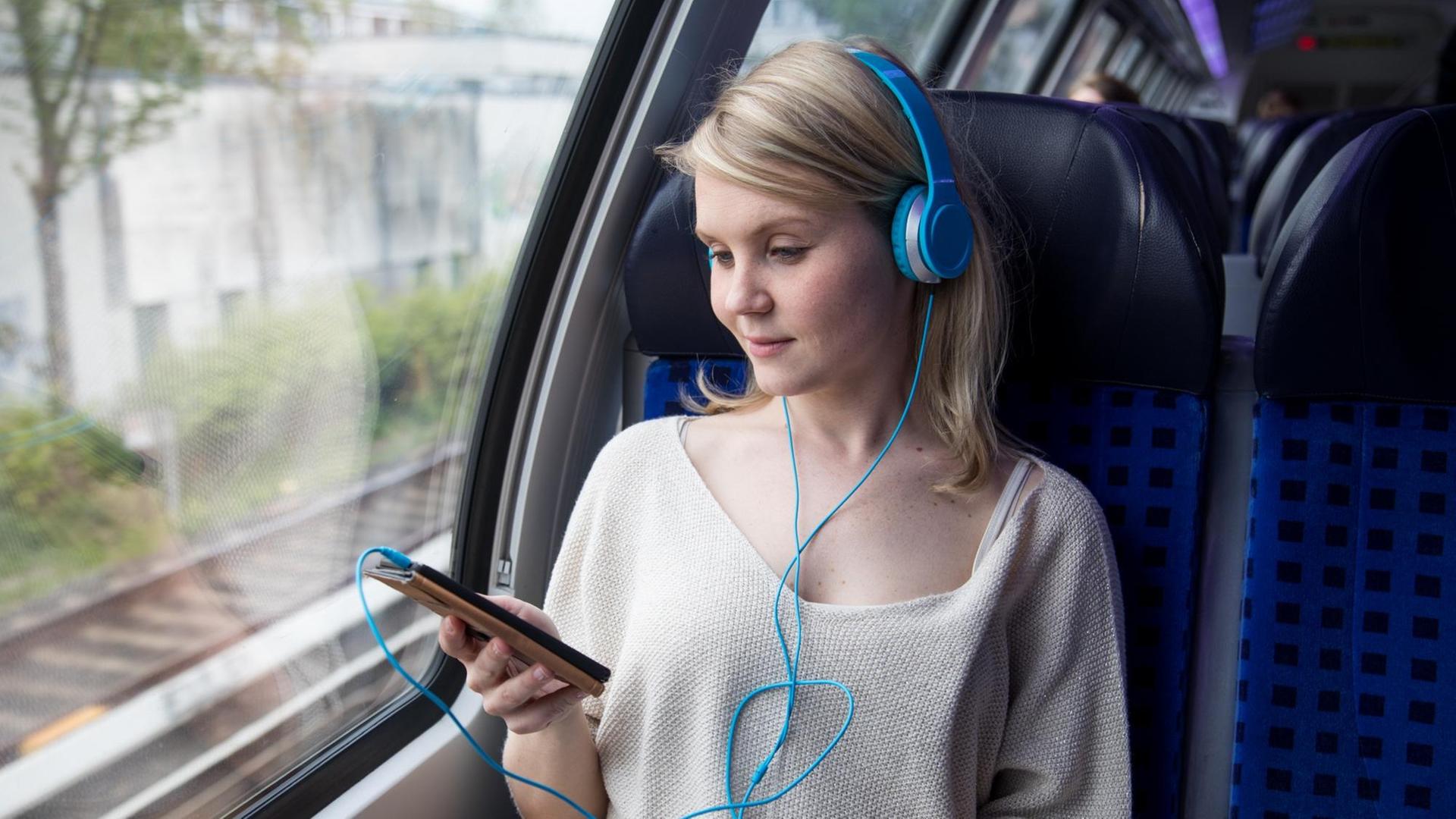 Eine Frau sitzt in einem Regionalexpress und schaut auf ihr Smartphone (gestellte Szene). Eine Frau sitzt in einem Regionalexpress und schaut auf ihr Smartphone (gestellte Szene).