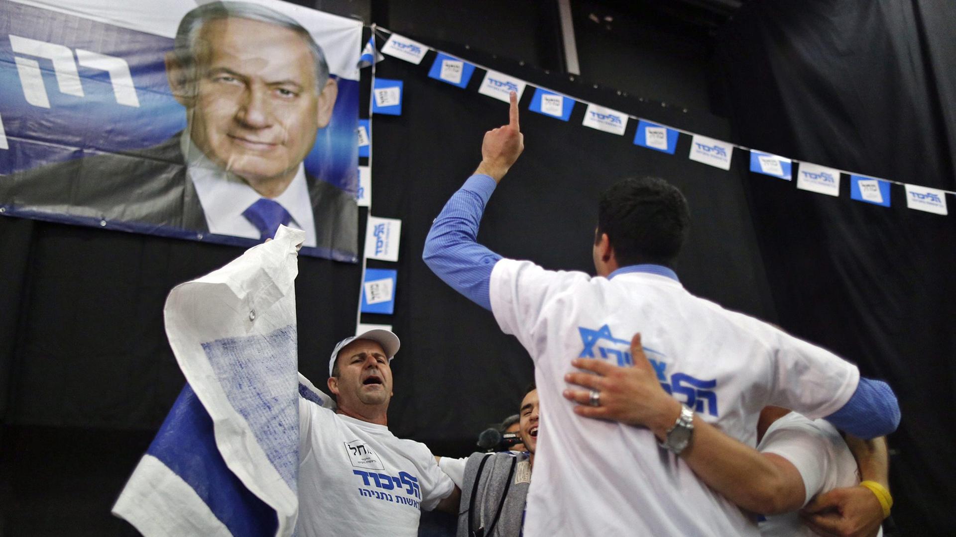 Männer mit Partei-T-Shirts bekleidet tanzen im Kreis unter einer Flagge mit dem Bild von Benjamin Netanjahu