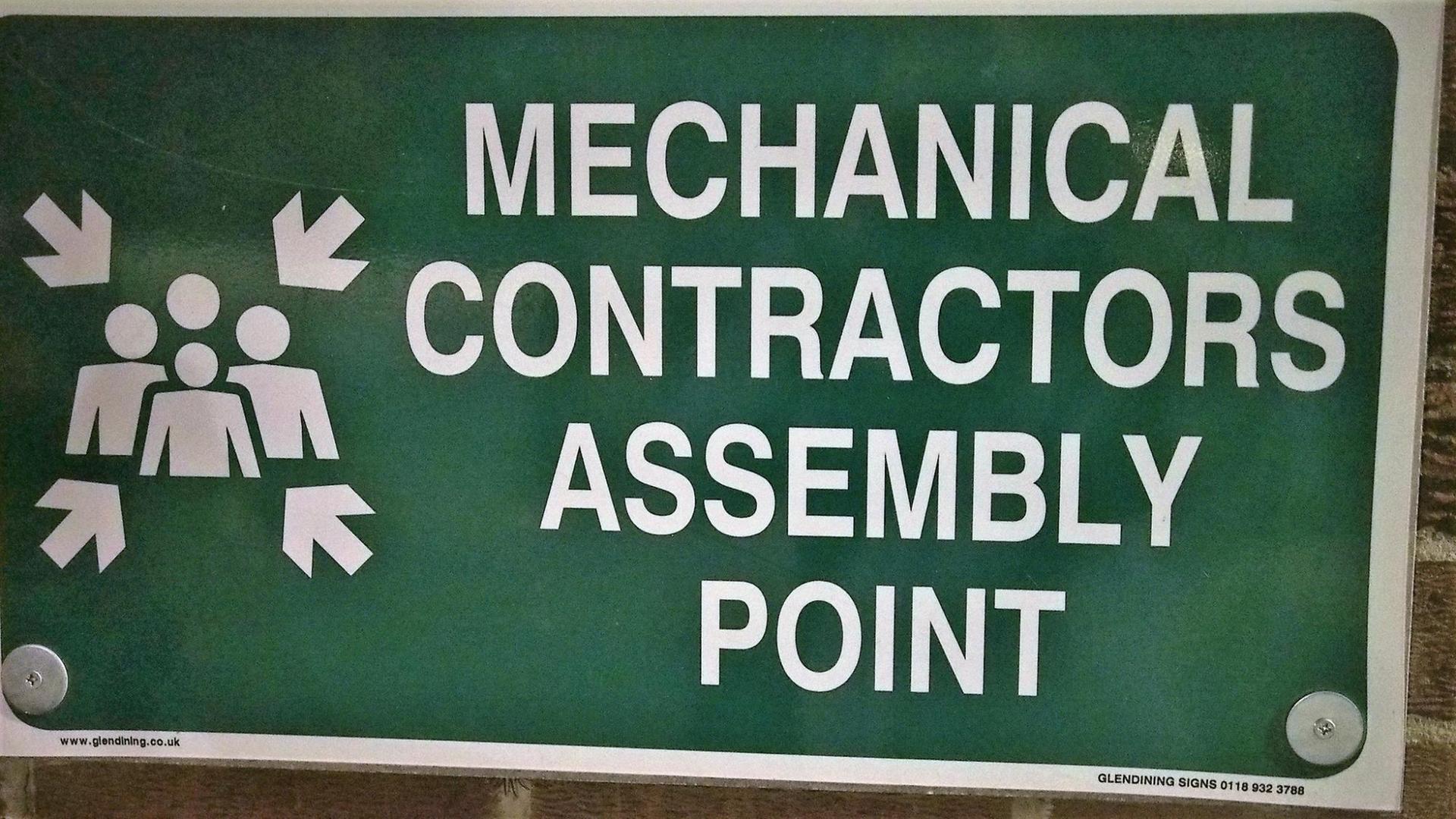 Ein Schild, dass bei Feuer oder anderen Gefahren, Arbeiter auf einen Sammelpunkt hinweist.