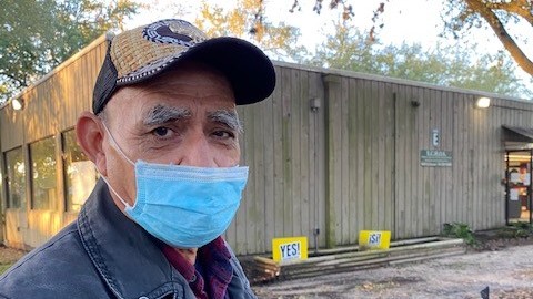 Ein älterer Mann mit Käppi, Jeansjacke und hellblauem Mundschutz steht vor einem Holzschuppen. Ein älterer Mann mit Käppi, Jeansjacke und hellblauem Mundschutz steht vor einem Holzschuppen.