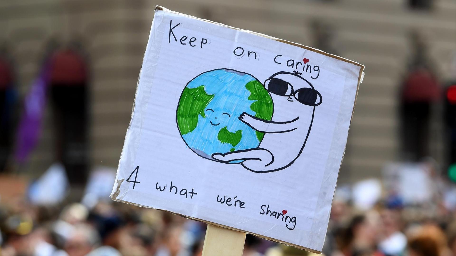 Klima-Demonstration im australischen Melbourne am 20. September 2019. Zu sehen ist ein Schild, das in die Höhe gehalten wird: Eine Figur umarmt die Erdkugel, darüber steht "Keep on caring".