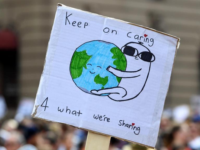 Klima-Demonstration im australischen Melbourne am 20. September 2019. Zu sehen ist ein Schild, das in die Höhe gehalten wird: Eine Figur umarmt die Erdkugel, darüber steht "Keep on caring".