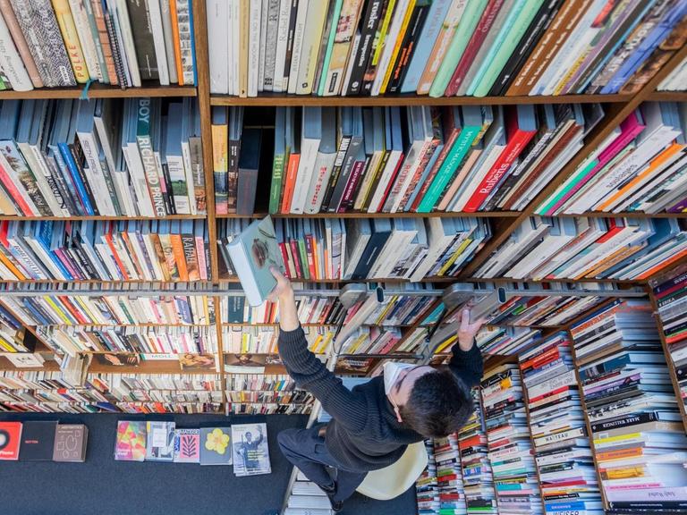 Ein Mitarbeiter der Buchhandlung Walther König steht auf einer Leiter vor einem Regal und sortiert Bücher ein. Die Verlagsbuchhandlung ist spezialisiert auf Kunst und Kunstwissenschaft, Architektur, Kunstgewerbe, Design, Mode, Fotografie, Film und Kunsttheorie sowie auf Ausstellungskataloge.