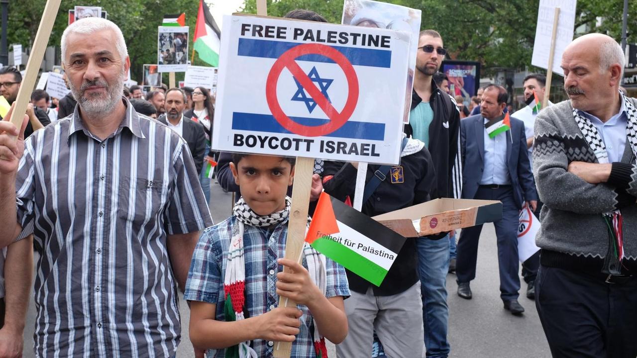 Ein Junge hält ein Schild hoch mit einem Boykott-Aufruf gegen Israel. Am Al-Kuds-Tag demonstrieren Palästinenser auf dem Berliner Kurfürstendamm gegen sogenannte Zionisten und gegen Israel. Ein Junge hält ein Schild hoch mit einem Boykott-Aufruf gegen Israel. Am Al-Kuds-Tag demonstrieren Palästinenser auf dem Berliner Kurfürstendamm gegen sogenannte Zionisten und gegen Israel.