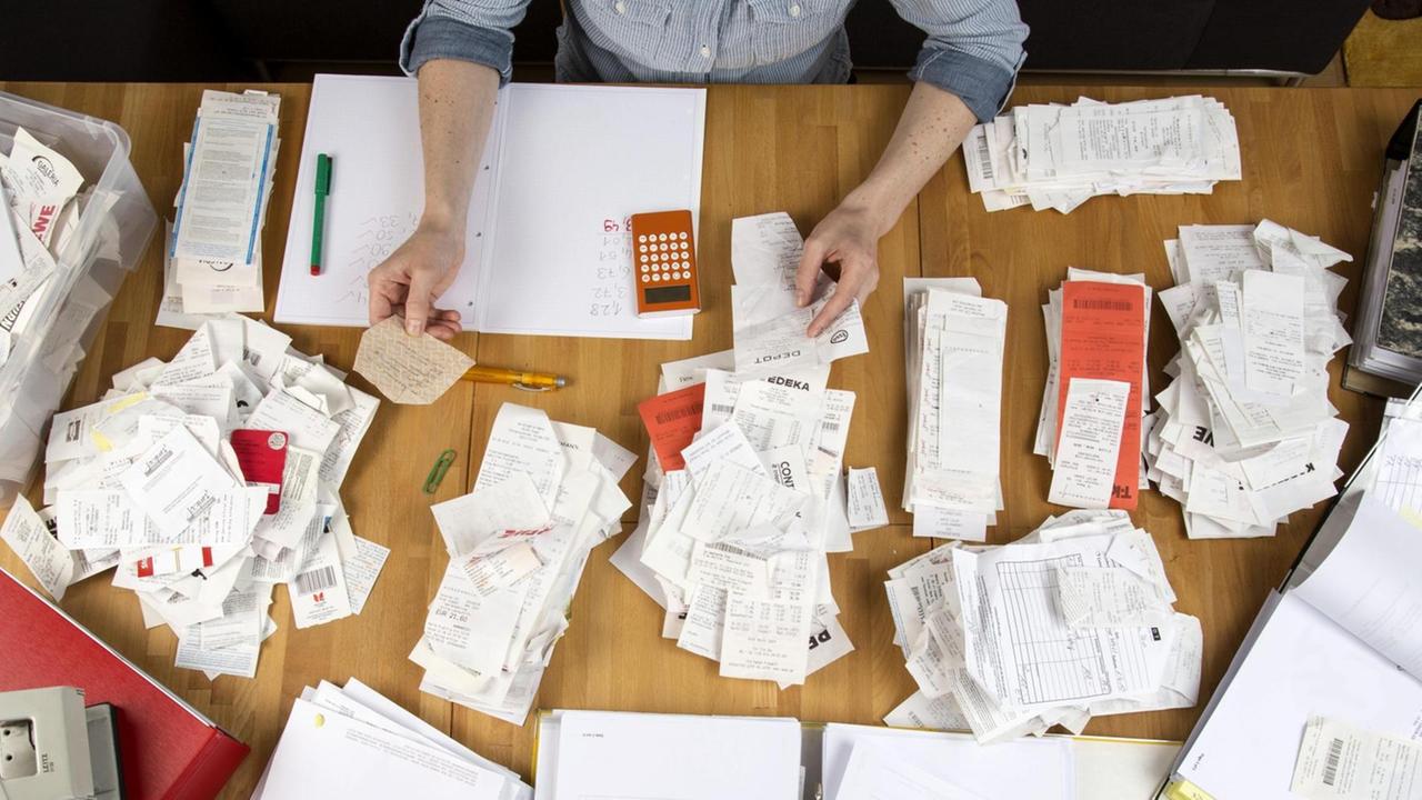 Frau sortiert Belege, Unterlagen, Rechnungen und Kassenbons auf einem Schreibtisch, für die Steuererklärung