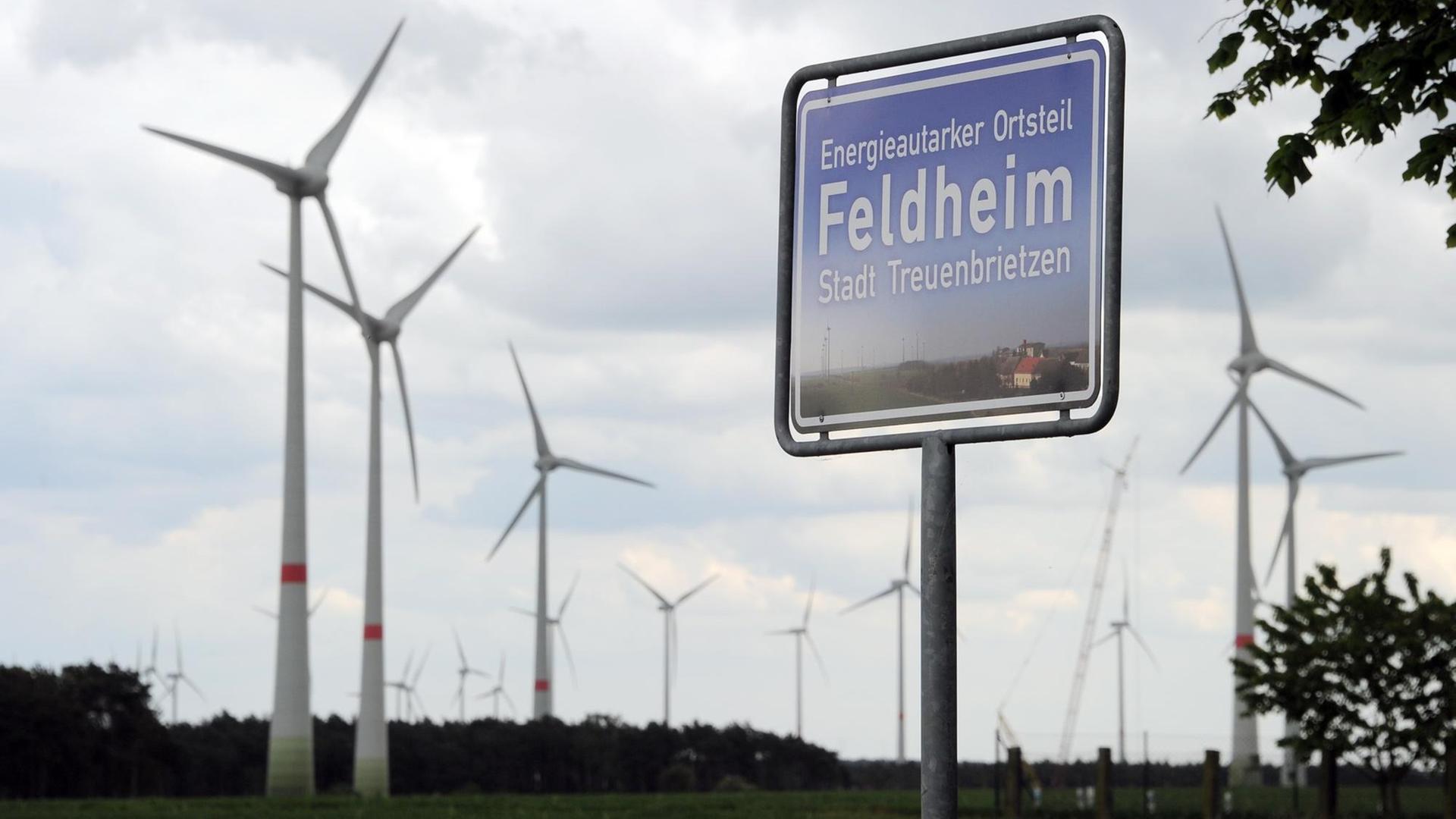 Ein blaues Schild, hinter dem sich Windräder drehen, weist Feldheim (Brandenburg) am 08.05.2014 als energieautarken Ort aus. Ein blaues Schild, hinter dem sich Windräder drehen, weist Feldheim (Brandenburg) am 08.05.2014 als energieautarken Ort aus.