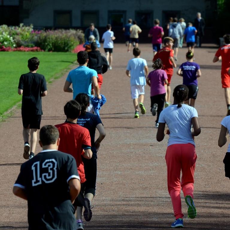 Schüler- und Schülerinnen laufen in Düsseldorf beim Schulsport durch eine Parkanlage. 