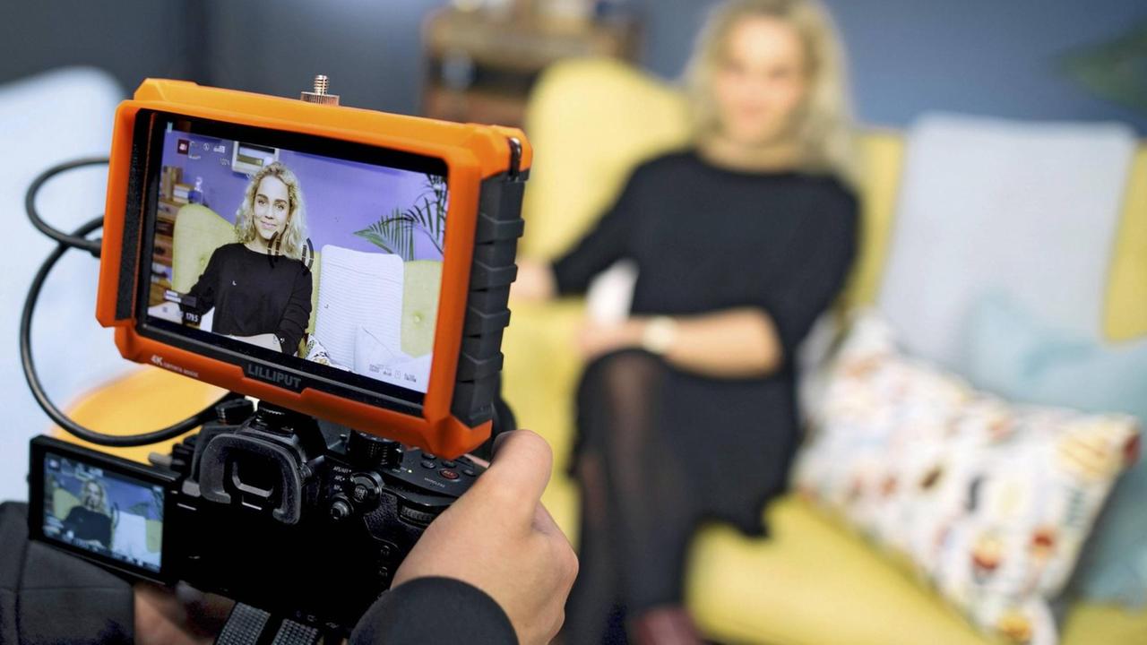 Die Youtuberin Jana Highholder sitzt auf einem gelben Sofa und wird von einer Kamera gefilmt. Die Youtuberin Jana Highholder sitzt auf einem gelben Sofa und wird von einer Kamera gefilmt.
