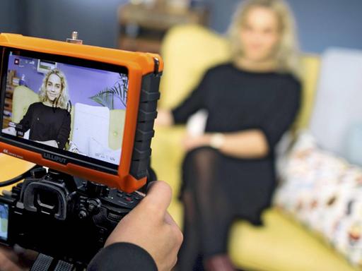 Die Youtuberin Jana Highholder sitzt auf einem gelben Sofa und wird von einer Kamera gefilmt.